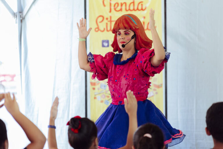 Apresentadora com figurino colorido anima crianças na Tenda Literária em Coroaci.