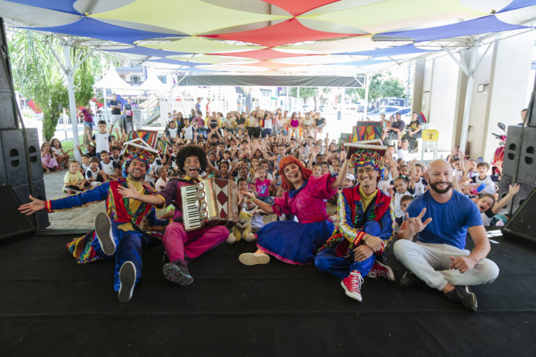 Imagem de artistas de teatro e música em apresentação ao ar livre durante o Festival Tenda Literária.