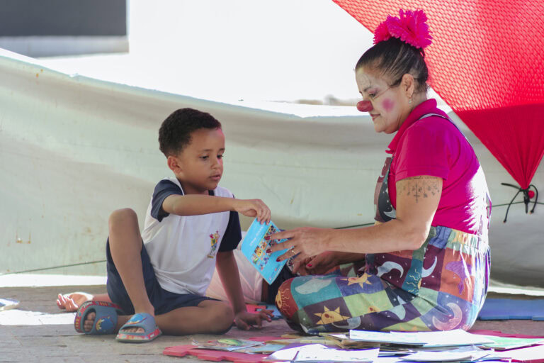 Espectador infantil e palhaça interagindo na Tenda Literária em Coroaci.