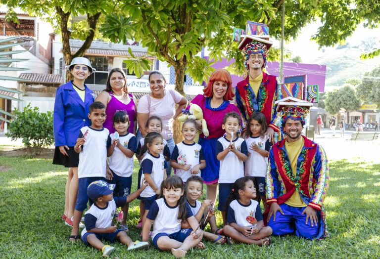 Imagem de crianças e adultos participando do Festival Tenda Literária em Coroaci, com palhaços e ati.