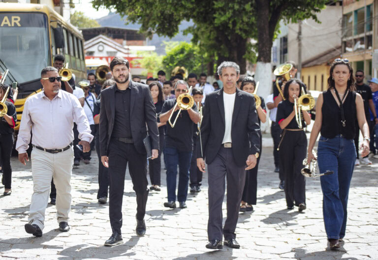 Encontro de bandas de música de Antônio Dias com músicos tocando instrumentos ao ar livre.