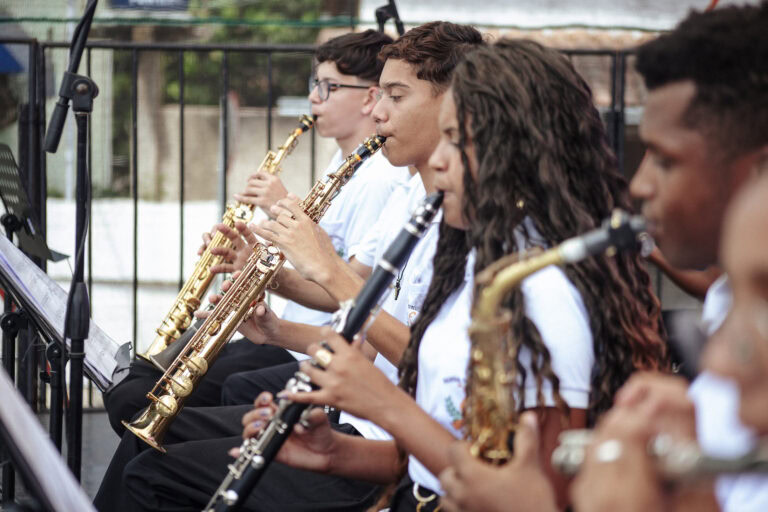 Banda de música de Antônio Dias tocando em evento escolar ao ar livre.