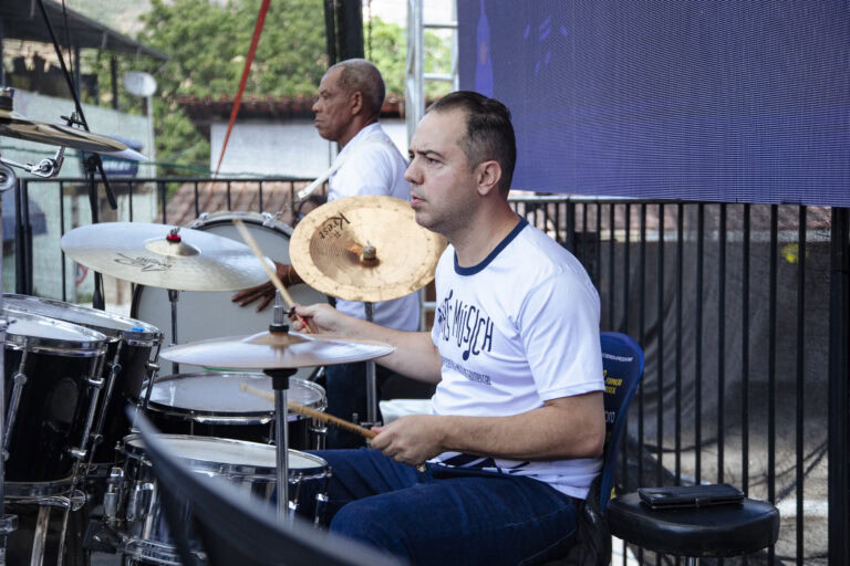 Banda de música tocando em evento de Antônio Dias, com músicos profissionais e instrumentos musicais.