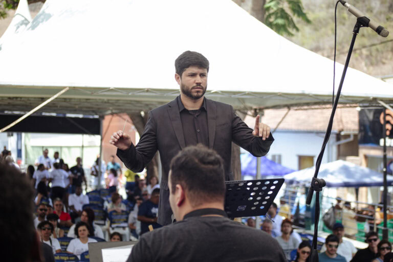 Diretor de orquestra conduz apresentação ao ar livre em evento cultural.