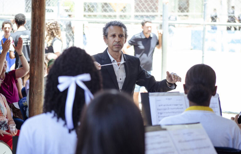 Encontro de bandas de música de Coronel Fabriciano com maestro conduzindo a orquestra ao ar livre.