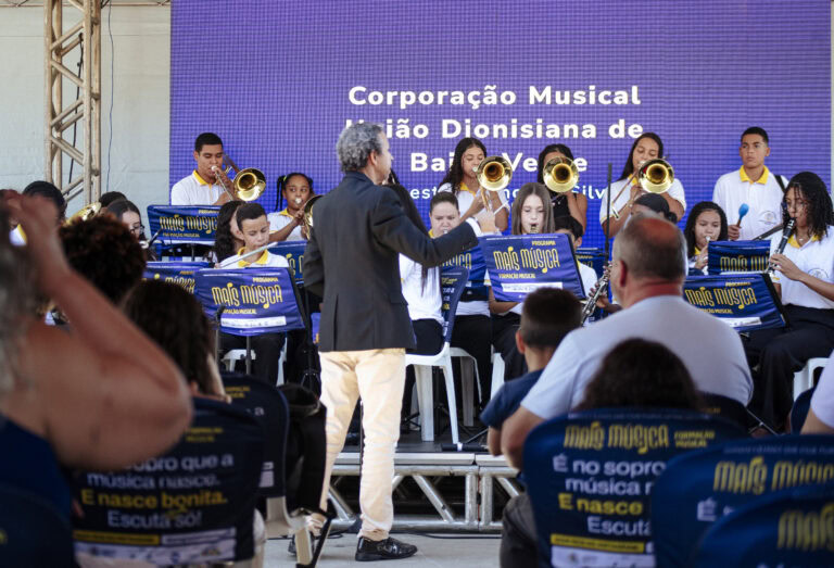 Banda de música em apresentação no encontro de Coronel Fabriciano, com maestro conduzindo e público.