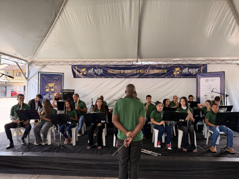 Encontro de bandas de música de Coroaci com músicos tocando instrumentos em palco ao ar livre.