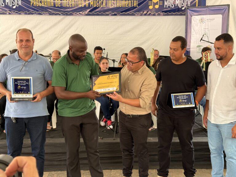 Imagem de homenagem durante o Encontro de Bandas de Música de Coroaci, com músicos recebendo certifi.