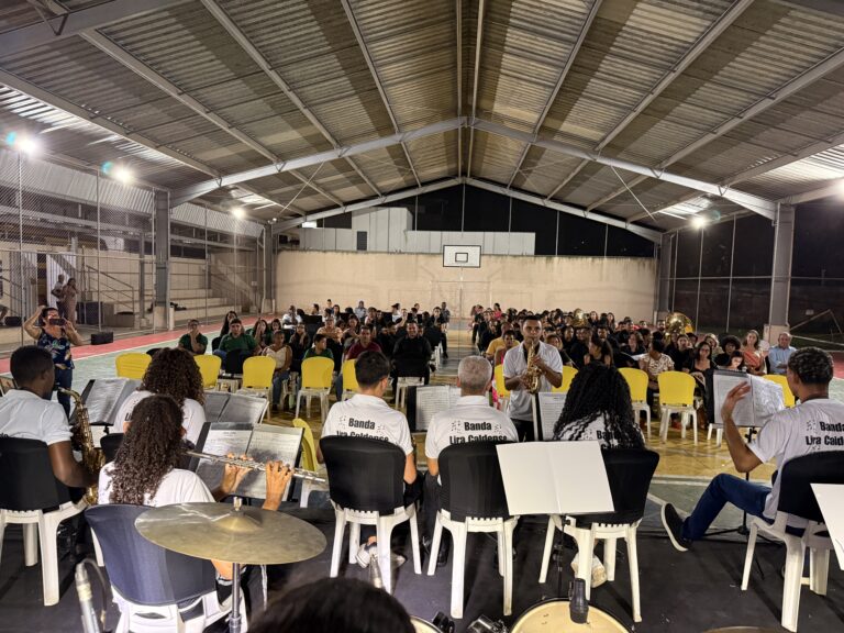 Encontro de bandas de música no ginásio de esportes de Naque, com músicos tocando instrumentos em ev.