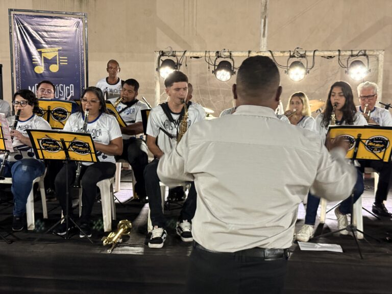 Encontro de bandas de música do Naque com jovens músicos tocando instrumentos em palco.