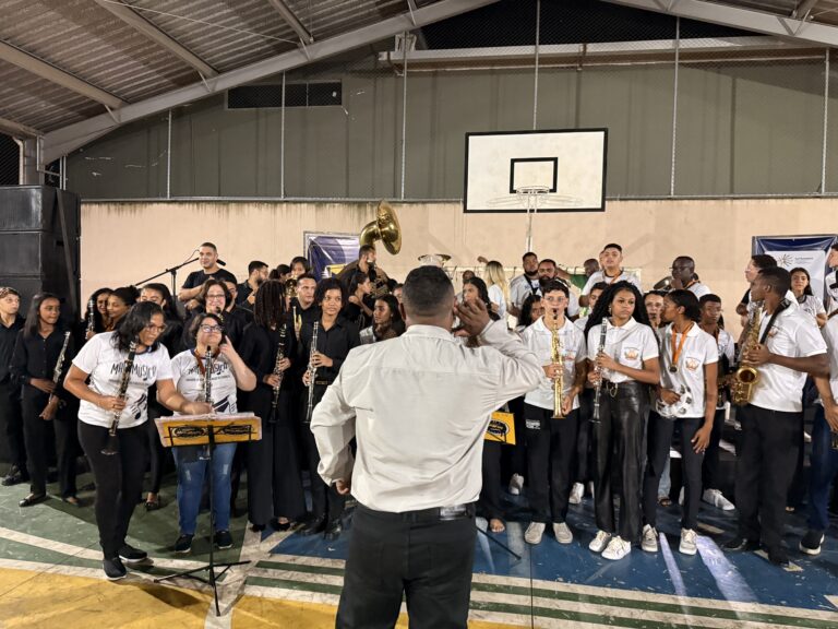 Encontro de bandas de música do Naque com jovens músicos e maestro em apresentação ao ar livre.