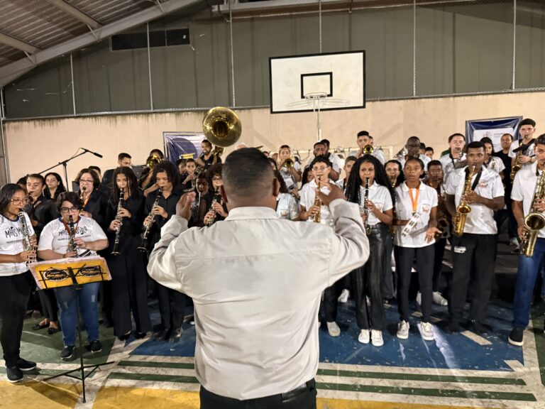 Encontro de bandas de música do Naque com jovens músicos tocando instrumentos em ginásio esportivo.