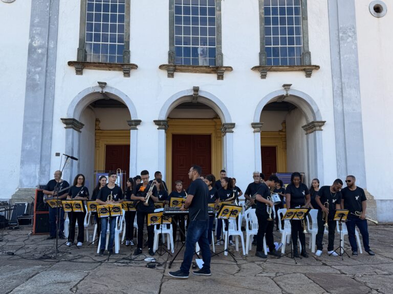 Encontro de bandas de música em Catas Altas, com músicos tocando ao ar livre na frente de uma igreja.