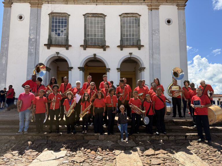 Encontro de bandas de música em Catas Altas com músicos em uniforme vermelho na frente de uma igreja.