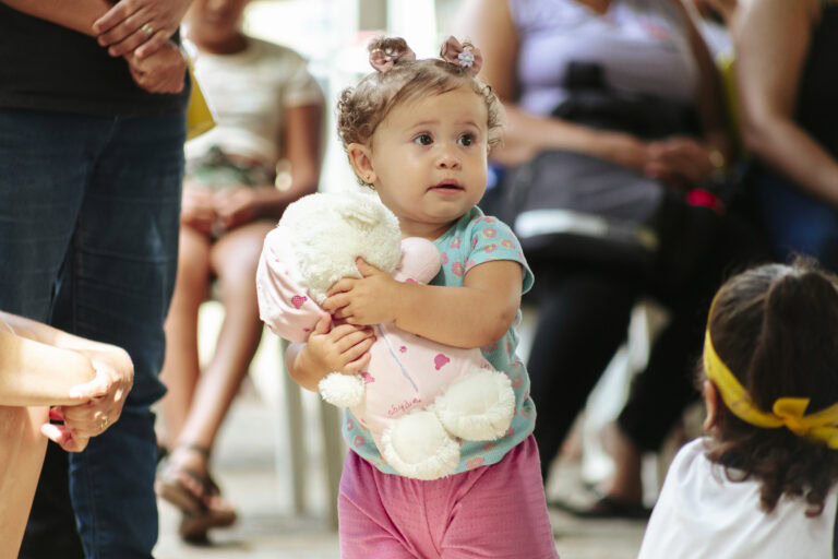 Criança segurando ursinho durante o Festival Tenda Literária Coroaci, evento cultural com atividades.