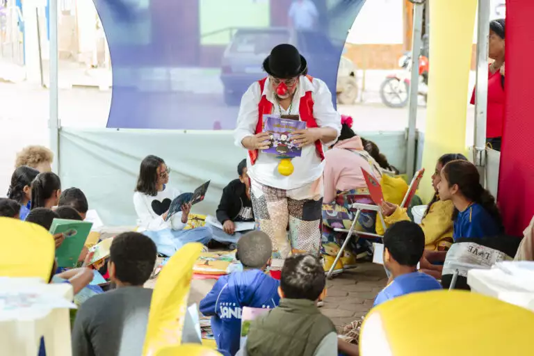Ator de palhaço entretém crianças durante evento literário ao ar livre.