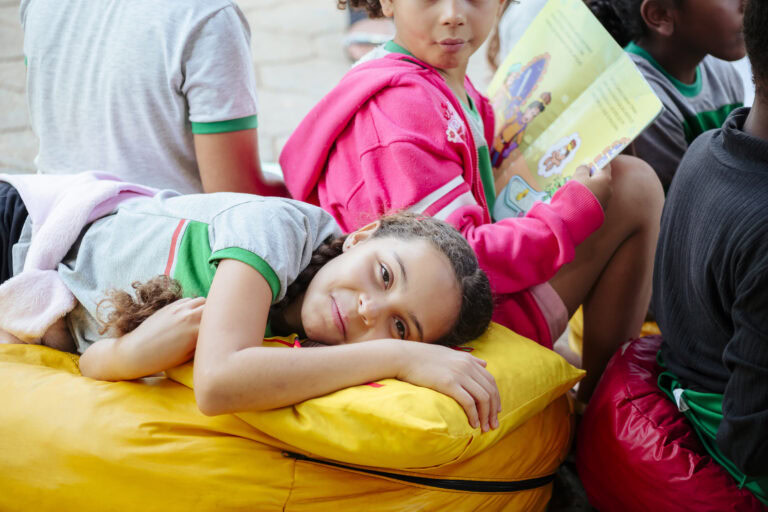 Imagem de uma criança deitada em almofada amarela, participando do Festival Tenda Literária Rio Verm.