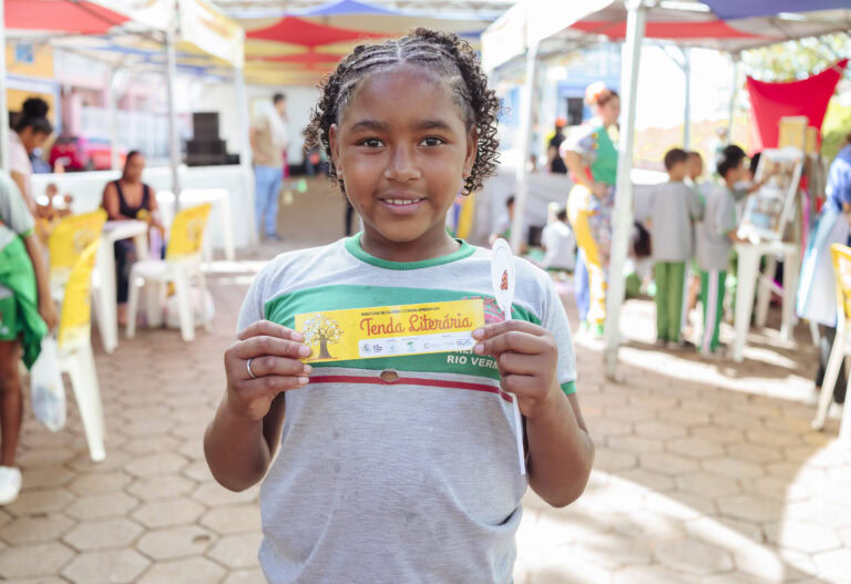 Imagem de uma criança sorridente segurando cartaz na Tenda Literária Rio Vermelho, evento cultural c.