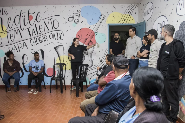 Grupo participando de aula especial de tambatuques, com instrutora e espectadores atentos.