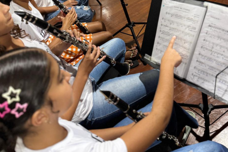 Imagem de crianças tocando instrumentos de sopro em aula de música.