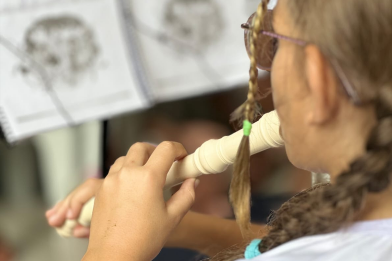 Aluna tocando flauta doce em aula de música para crianças.