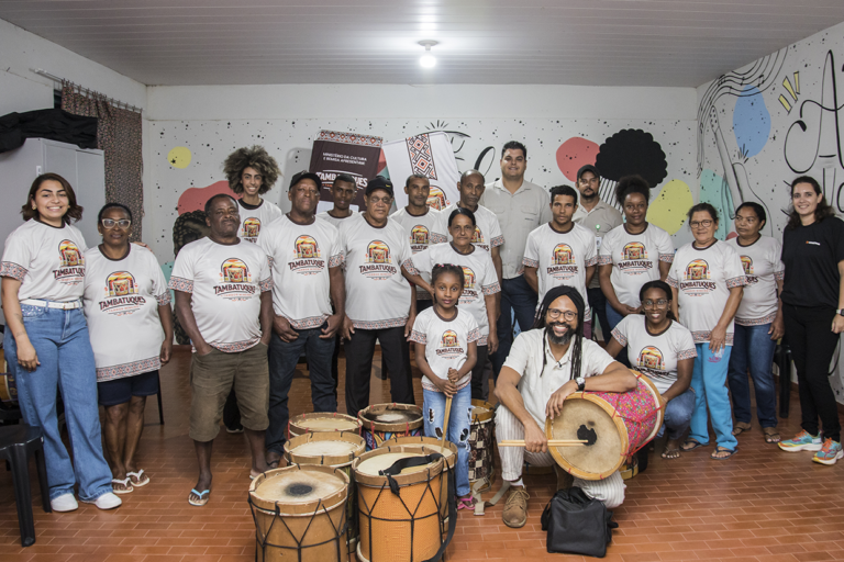 Aula de tambatuques com grupo diverso em atividade cultural e musical.