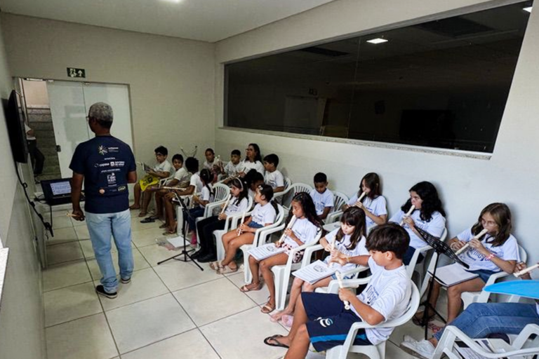 Aula de flauta doce para crianças em ambiente escolar, com instrutor orientando os alunos na prática.
