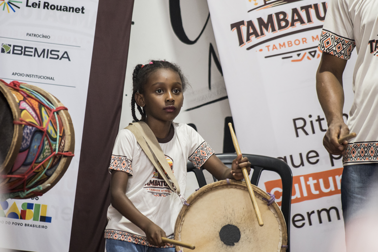 Imagem de uma menina tocando tambor em aula de tambatuques.
