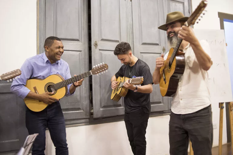 Imagem de músicos tocando violas em apresentação ao vivo.