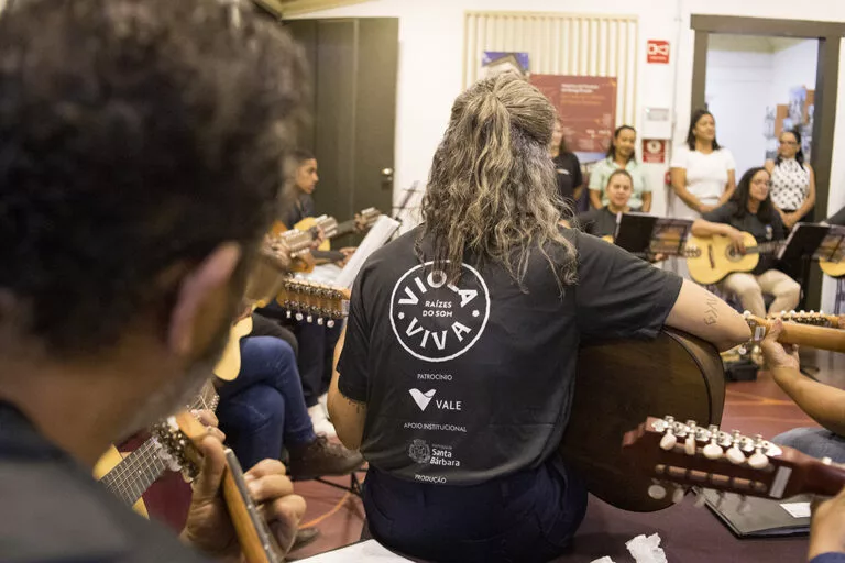 Imagem de músicos tocando violas em ensaio ou apresentação ao vivo.
