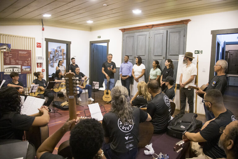 Imagem de músicos e participantes em apresentação de viola viva em evento especial.