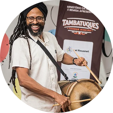Homem tocando tambor tradicional de Tambauques em evento cultural.