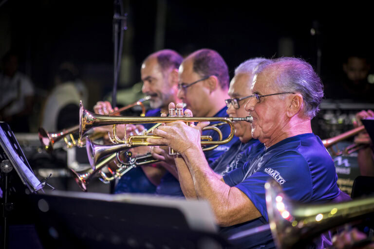 Músicos tocando trompetes em apresentação ao vivo.