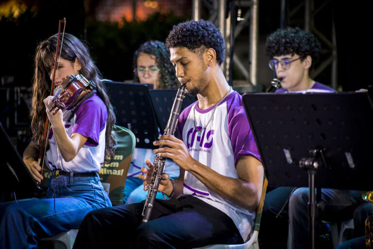 Jovens músicos tocando instrumentos em apresentação ao ar livre.
