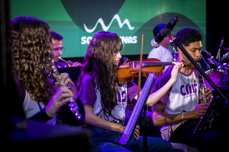 Jovens músicos tocando instrumentos de orquestra em apresentação ao vivo.