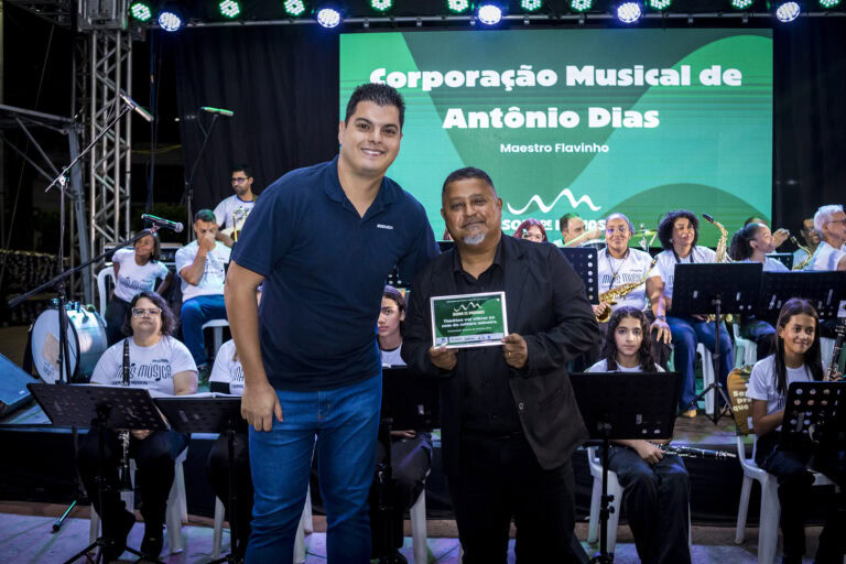 Homenagem à corporação musical de Antônio Dias em evento ao vivo.
