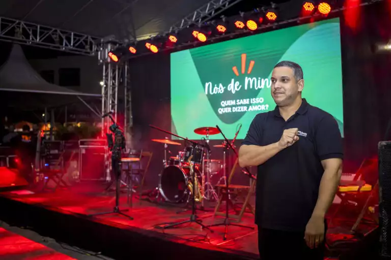 Apresentador em palco do evento Som de Minas com instrumentos musicais ao fundo.