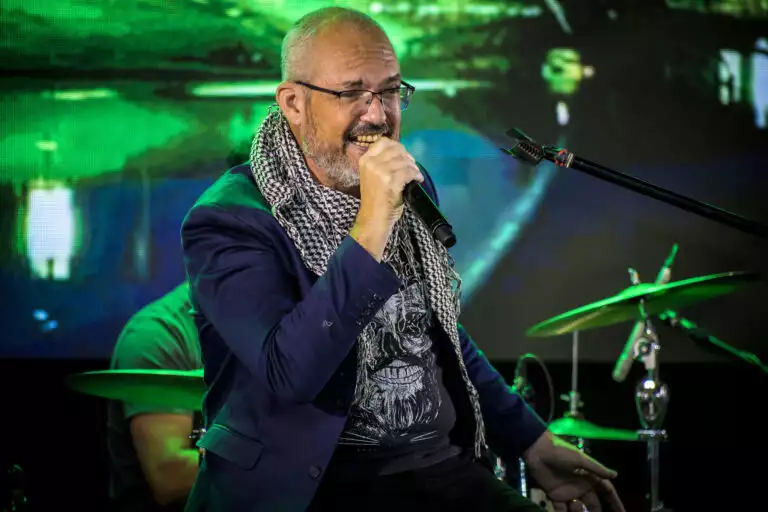 Homem cantando com microfone em show ao vivo, cenário de palco com iluminação verde.
