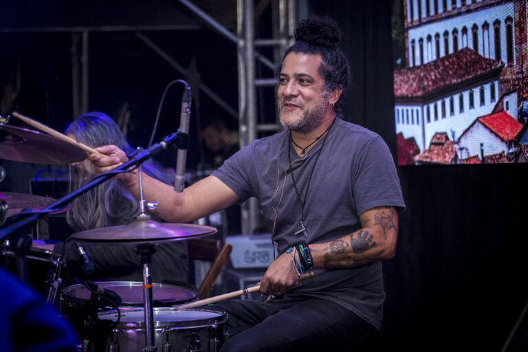 Baterista tocando bateria em show ao vivo com iluminação e palco.
