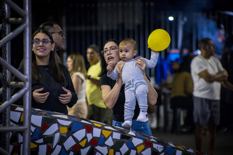 Família com criança segurando balão amarelo em evento cultural ao ar livre.