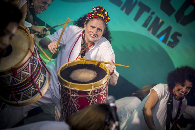 Mulher tocando tambor em apresentação cultural de Minas Gerais.