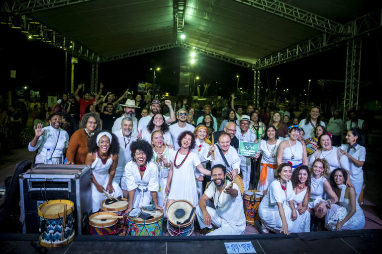 Grupo de músicos tocando instrumentos tradicionais em palco ao ar livre.
