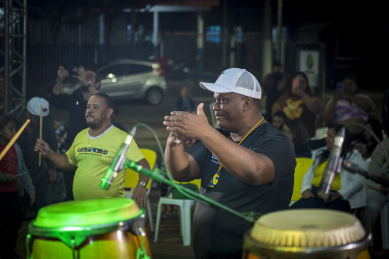 Homem tocando tambor no Festival Tambatuques com público ao fundo.